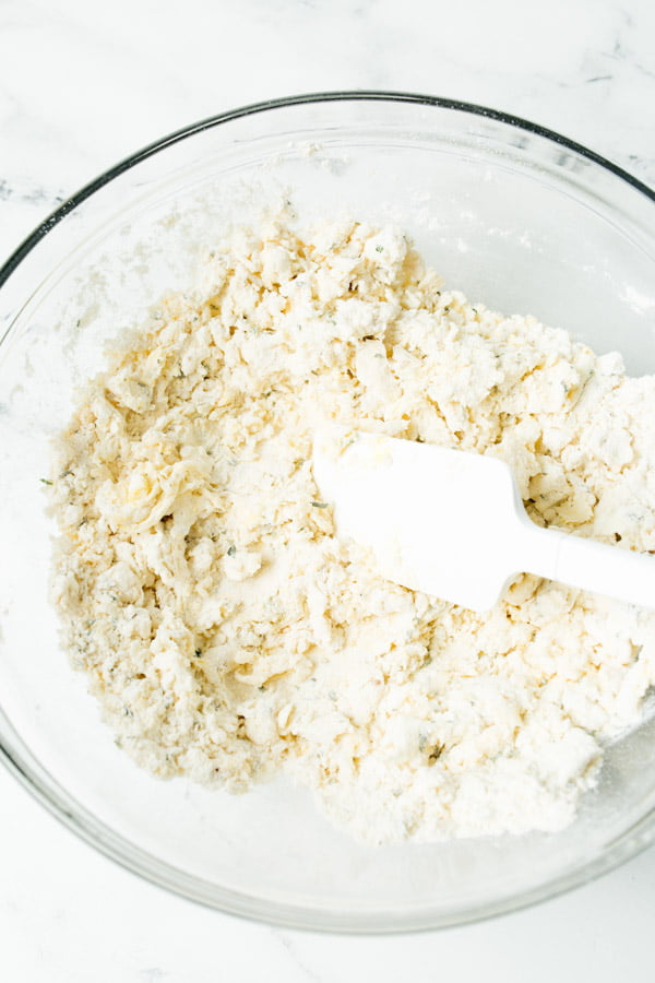 Loose breadstick dough in a glass bowl with a white rubber spatula.