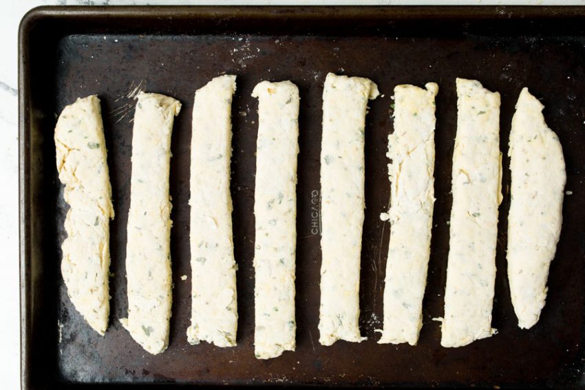 8 rustic breadsticks pre baked on a baking sheet.