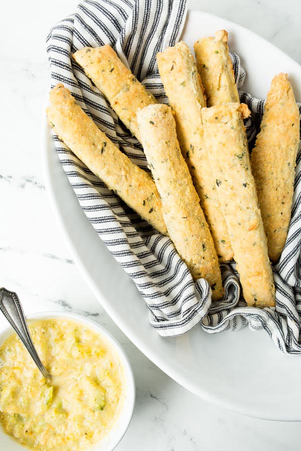 Homemade gluten free breadsticks in a bowl next to a bowl of broccoli cheddar soup. 