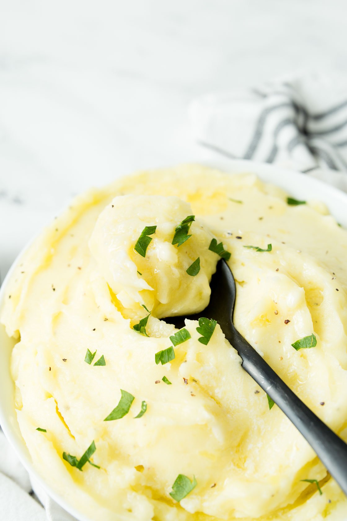 A black spoonful of mashed potatoes with parsley and black pepper
