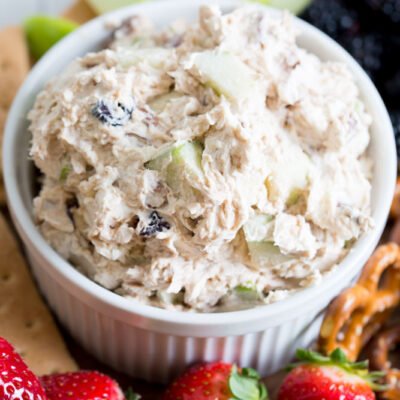 An image of cranberry walnut dip in a white ramkin on a wood board surrounded by fruits and crackers.